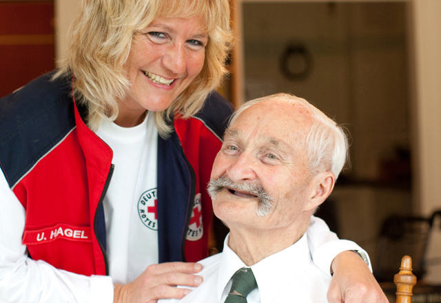Die DRK Tagespflege. Ein lachender Senior mit einer DRK Mitarbeiterin.
